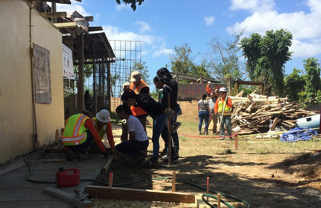 group of people fixing up hurricane-damaged building