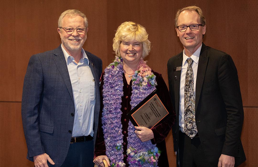 Lesley Blair poses with her award against wooden wall with Bob Mason and Roy Haggerty