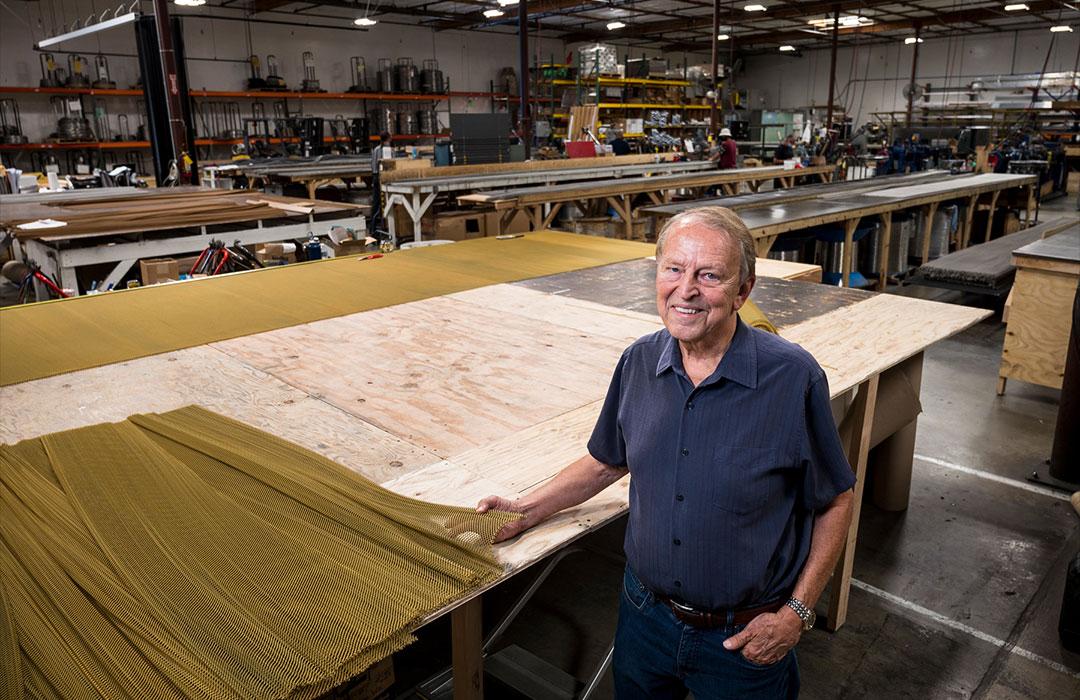 Man standing in front of a table in a factory with metal coil wire screening laying on it.