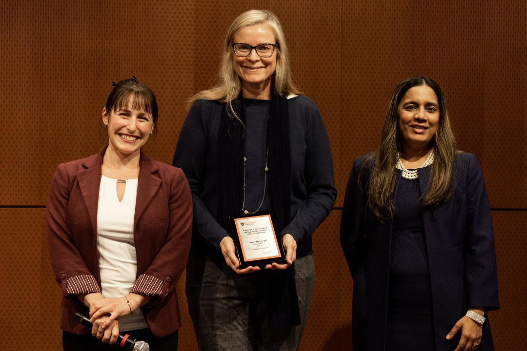 Mary Beisiegel standing in a black shirt and dark pants receiving a plaque. 