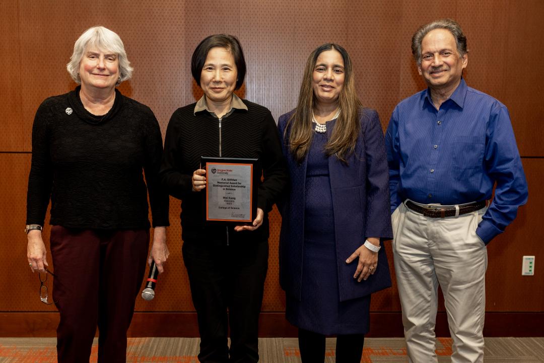 Four individuals pose for a picture. Wei Kong holds an award. 
