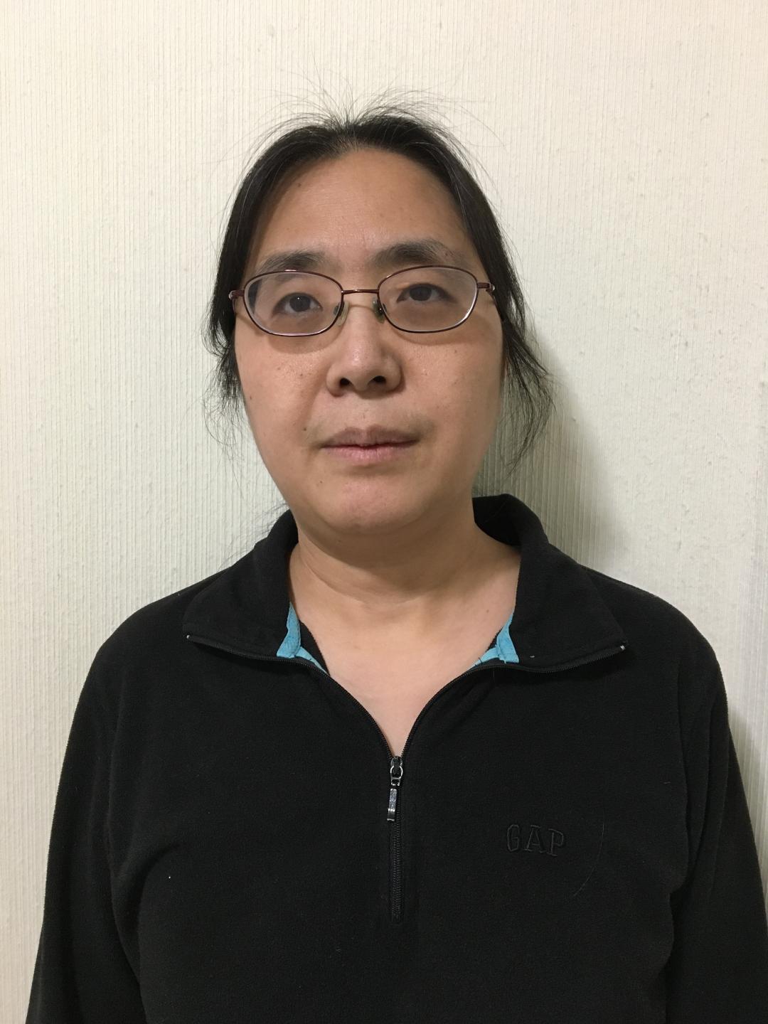 Zhen Yu stands in a black shirt in front of a plain wall. 