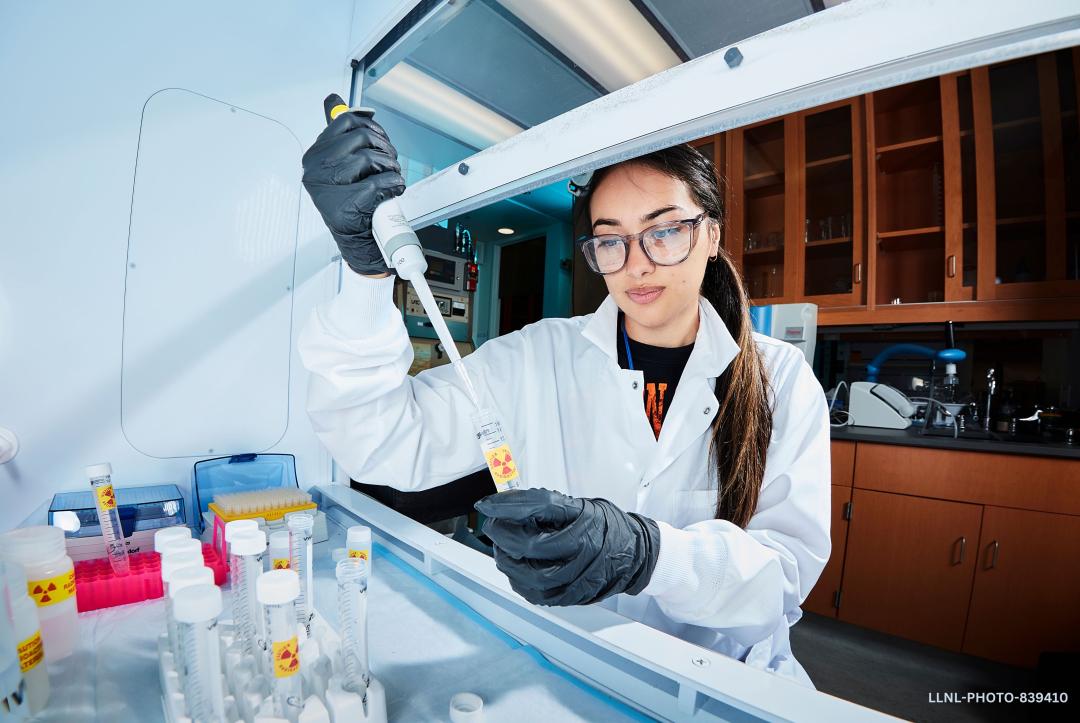 Bustos in the lab pipetting into containers with radioactive warning labels.