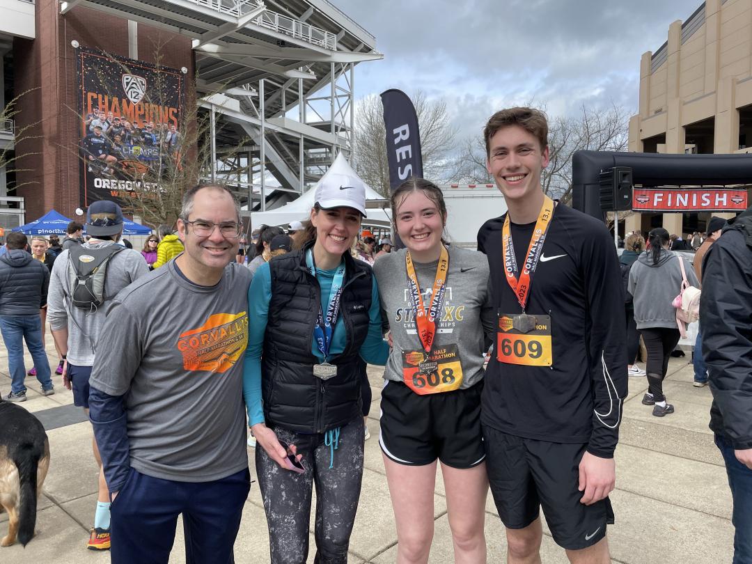 Four people stand with running bibs in front of the OSU football stadium.