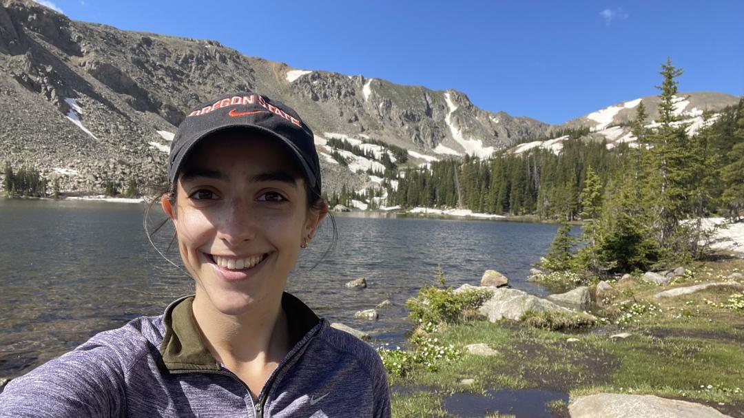 Sousa smiles in front of a crystal clear lake bordered by craggy mountainsides and pines.
