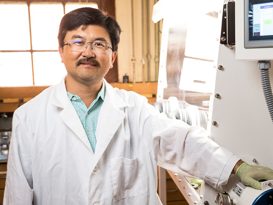A man in a white lab coat stands next to equipment in a laboratory at Oregon State College of Science.
