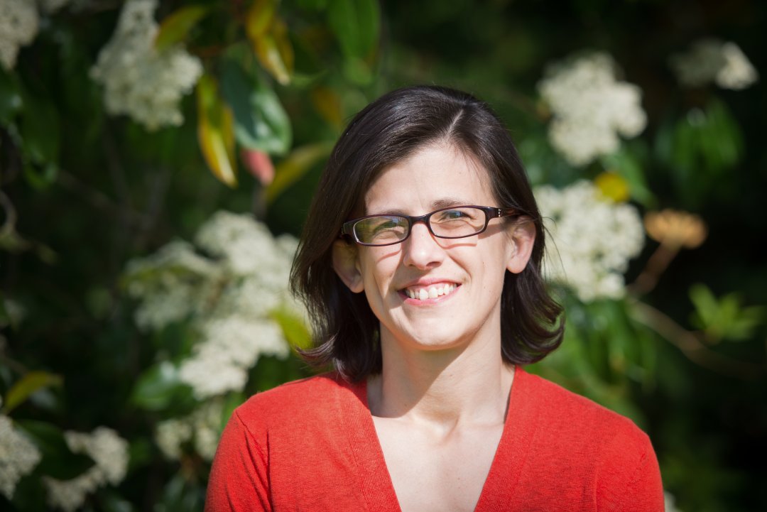 A woman in a red top poses in front of plants.