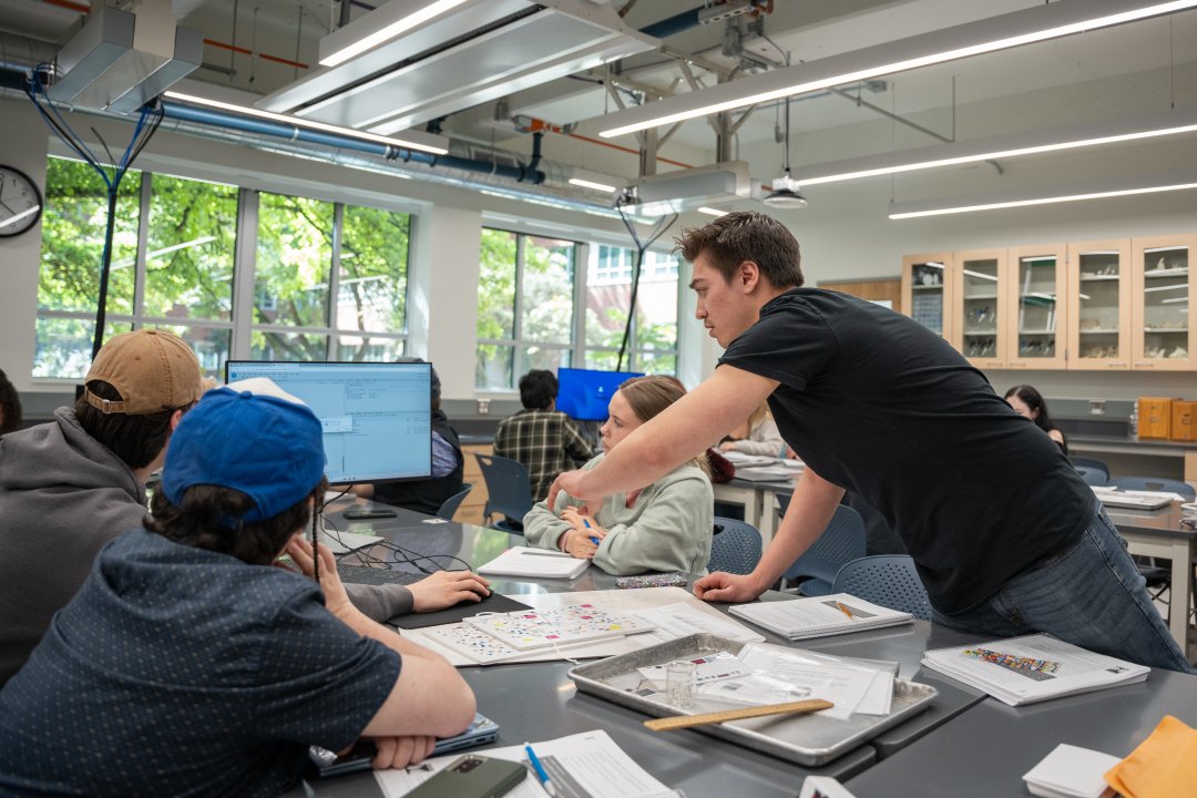 Students in a laboratory classroom point to a computer with data