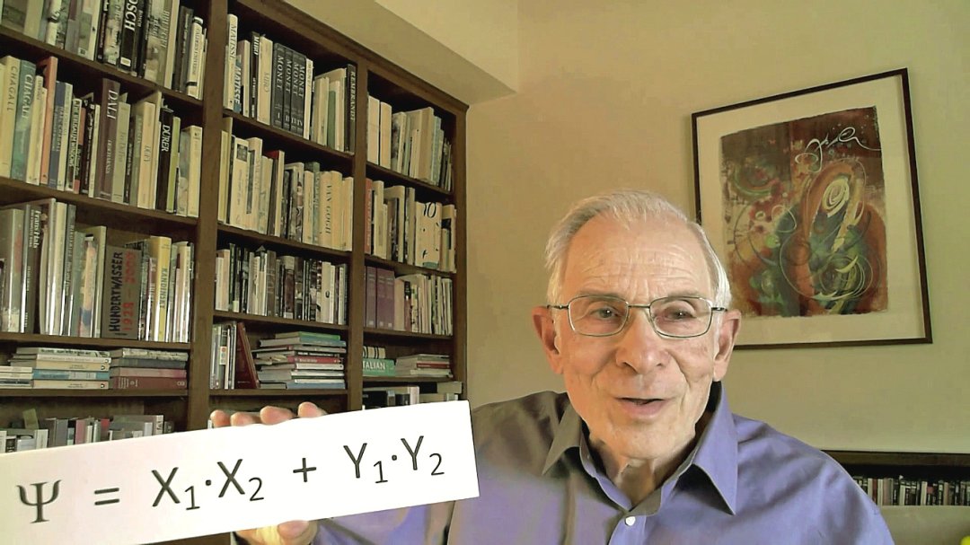 Carl Kocher in an office displaying a quantum physics equation while seated in front of bookshelves. 