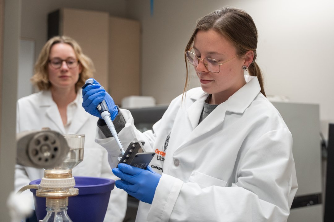 Two women in lab coats work with pipets.
