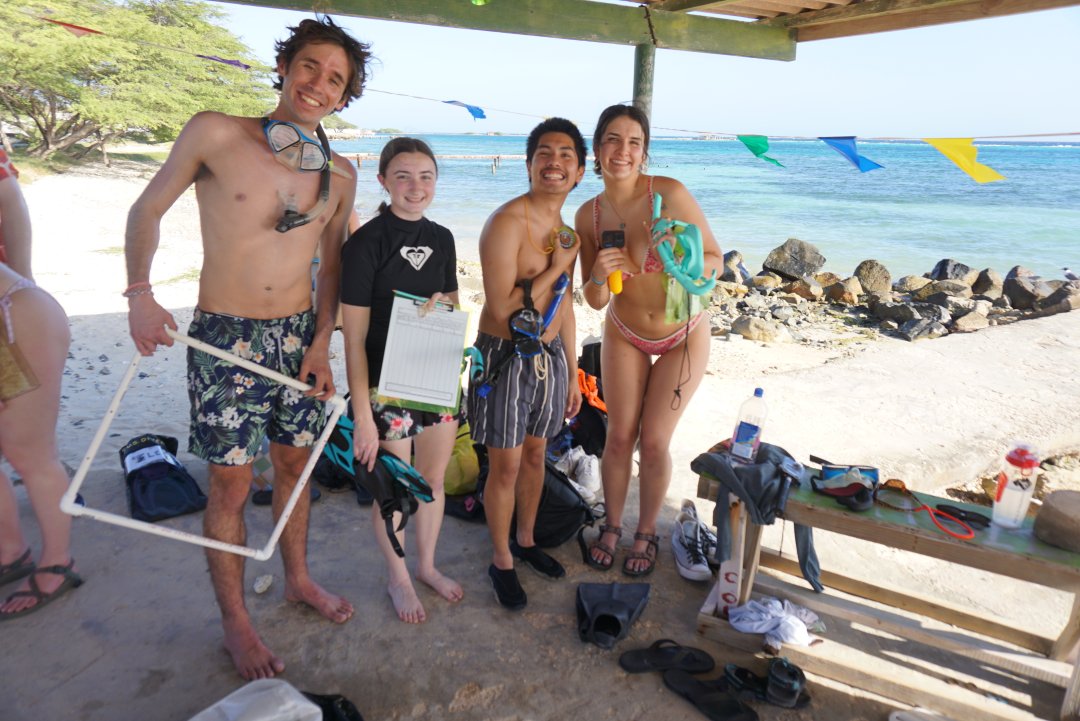 Students in swimsuits pose for a photo on a beach.