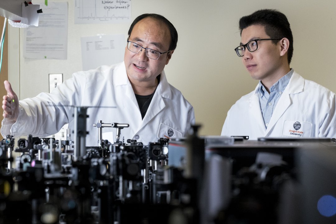 Two male researchers in lab coats look at lasers.