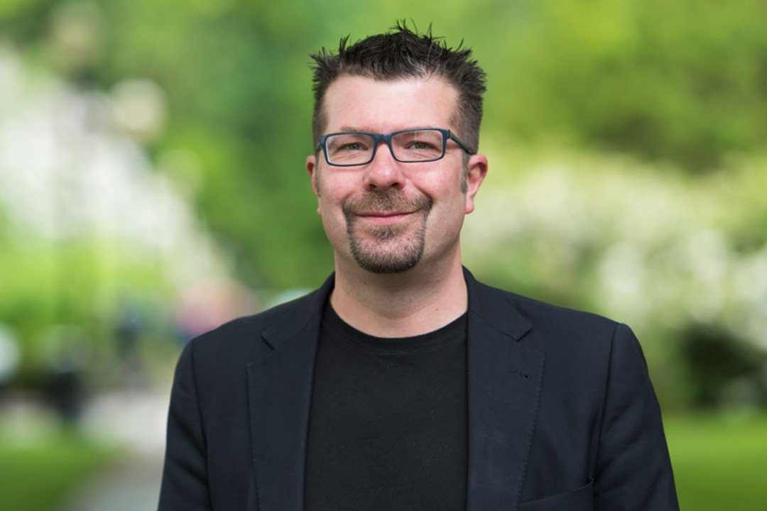 Headshot of a man wearing a black suit and glasses.