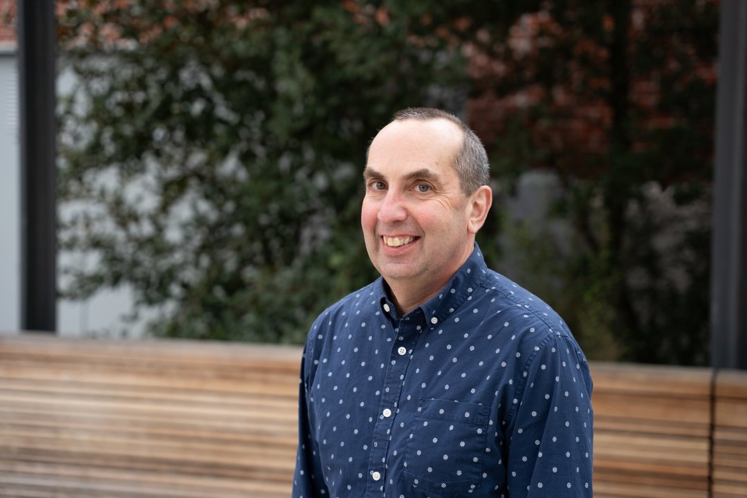 A man in a blue shirt with white polka dots poses for a headshot.