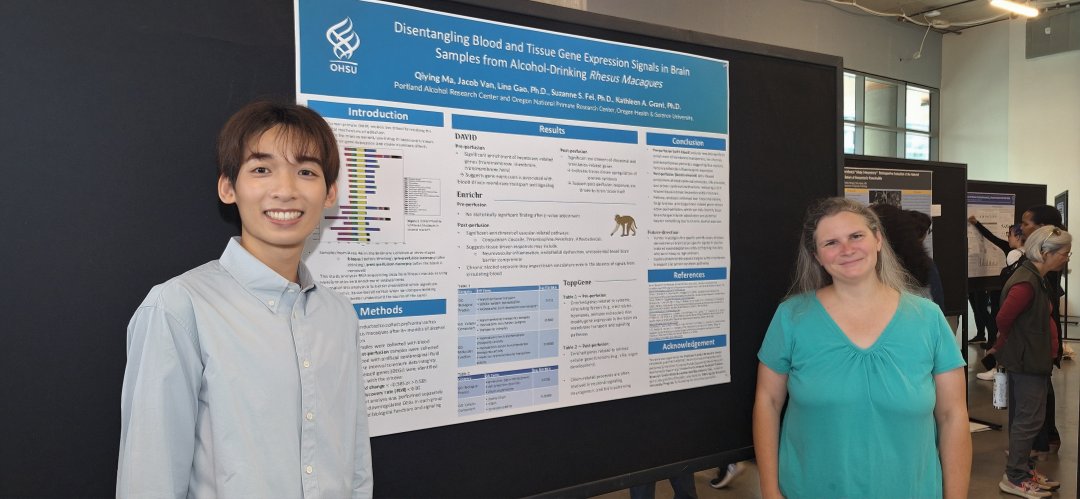 A man and a woman stand at both ends of a research poster, smiling at the camera. The man is in a button-up shirt and the woman is wearing a turquoise blouse.