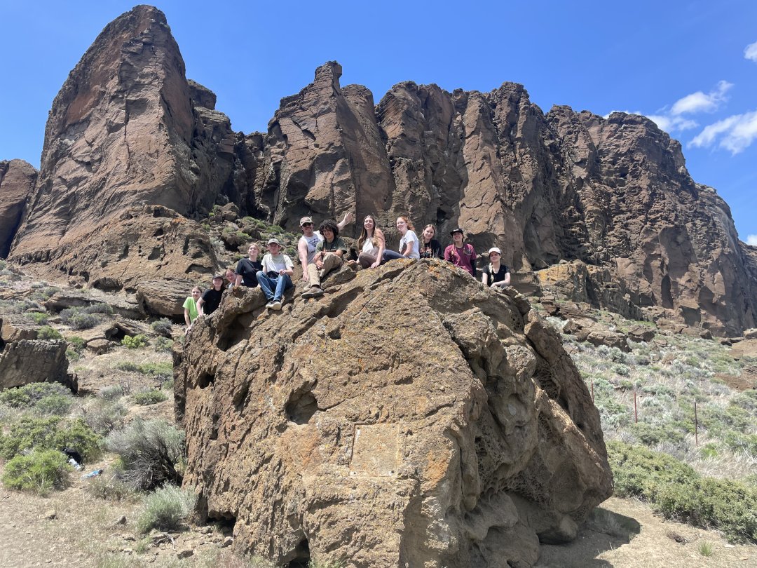 A large group of students pose for a photo sitting on a rock in the Oregon wilderness.