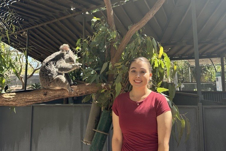 A woman stands next to a koala.