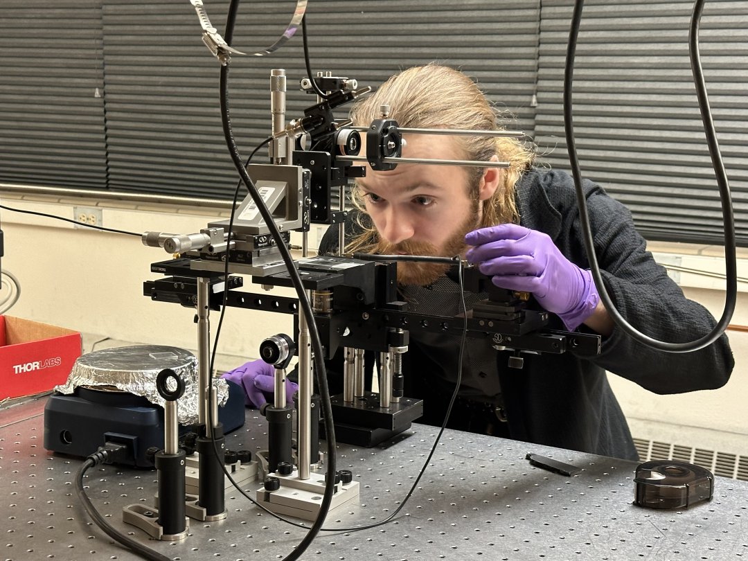 A man in a lab coat and gloves works with lasers in a laboratory. 