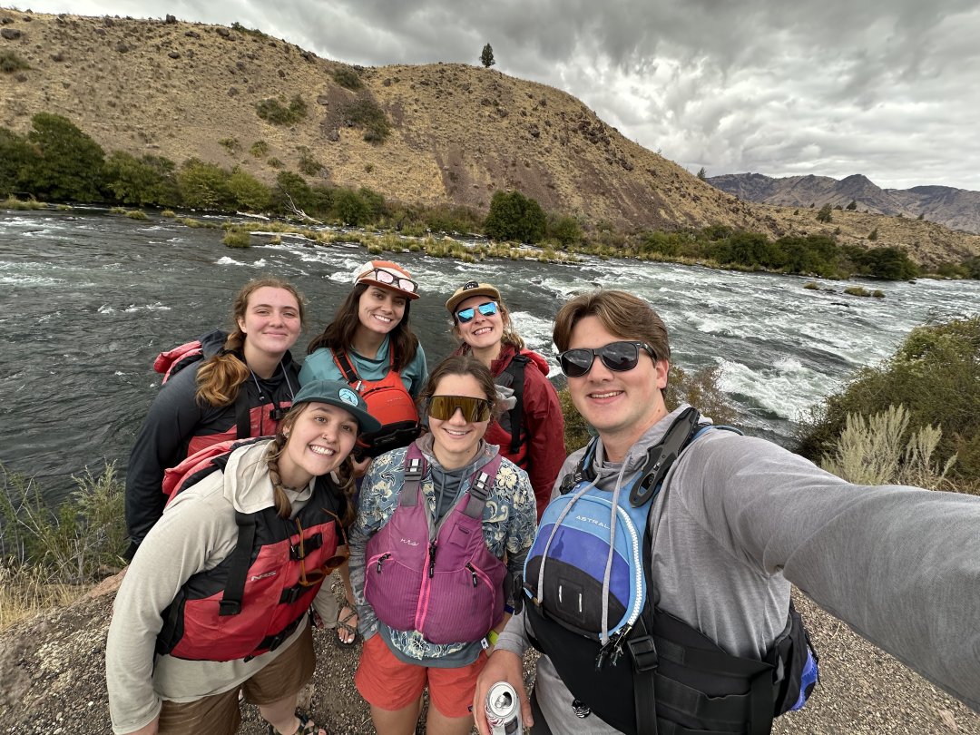 A group of people wearing life jackets pose for a photo while on a river rafting adventure.