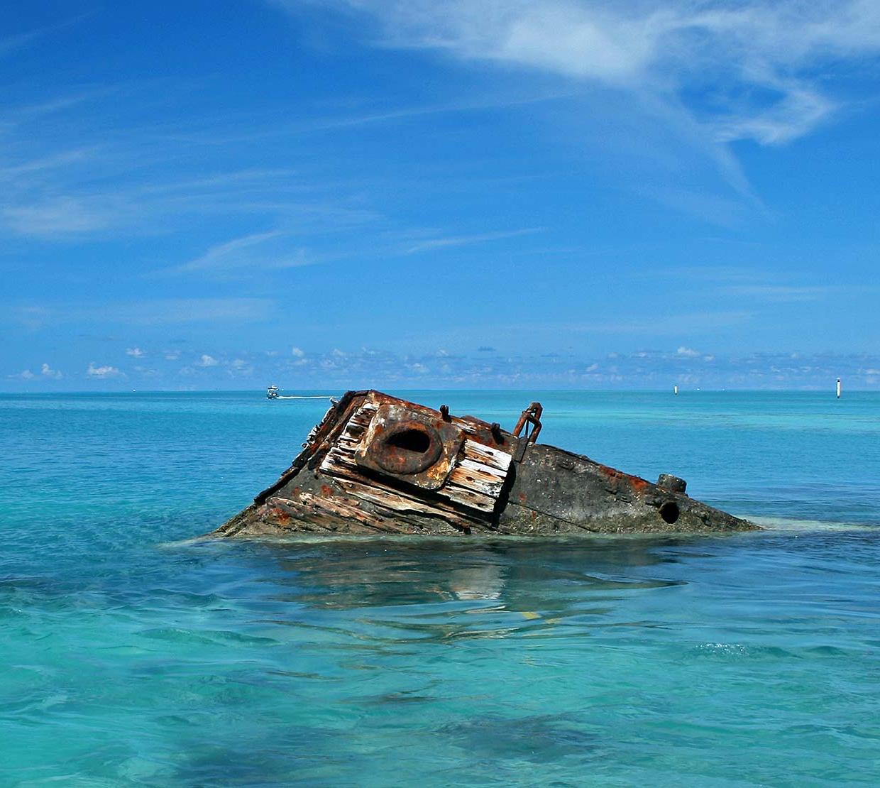 sunken ship peering above surface of ocean on a sunny day