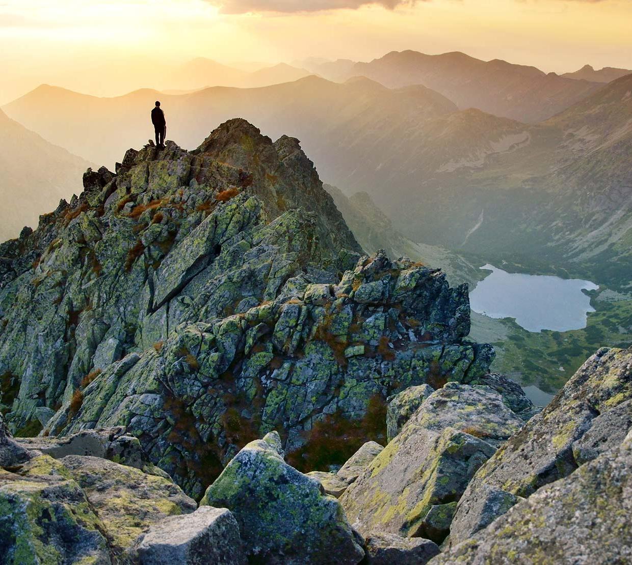 Person standing atop mountain in mountain range