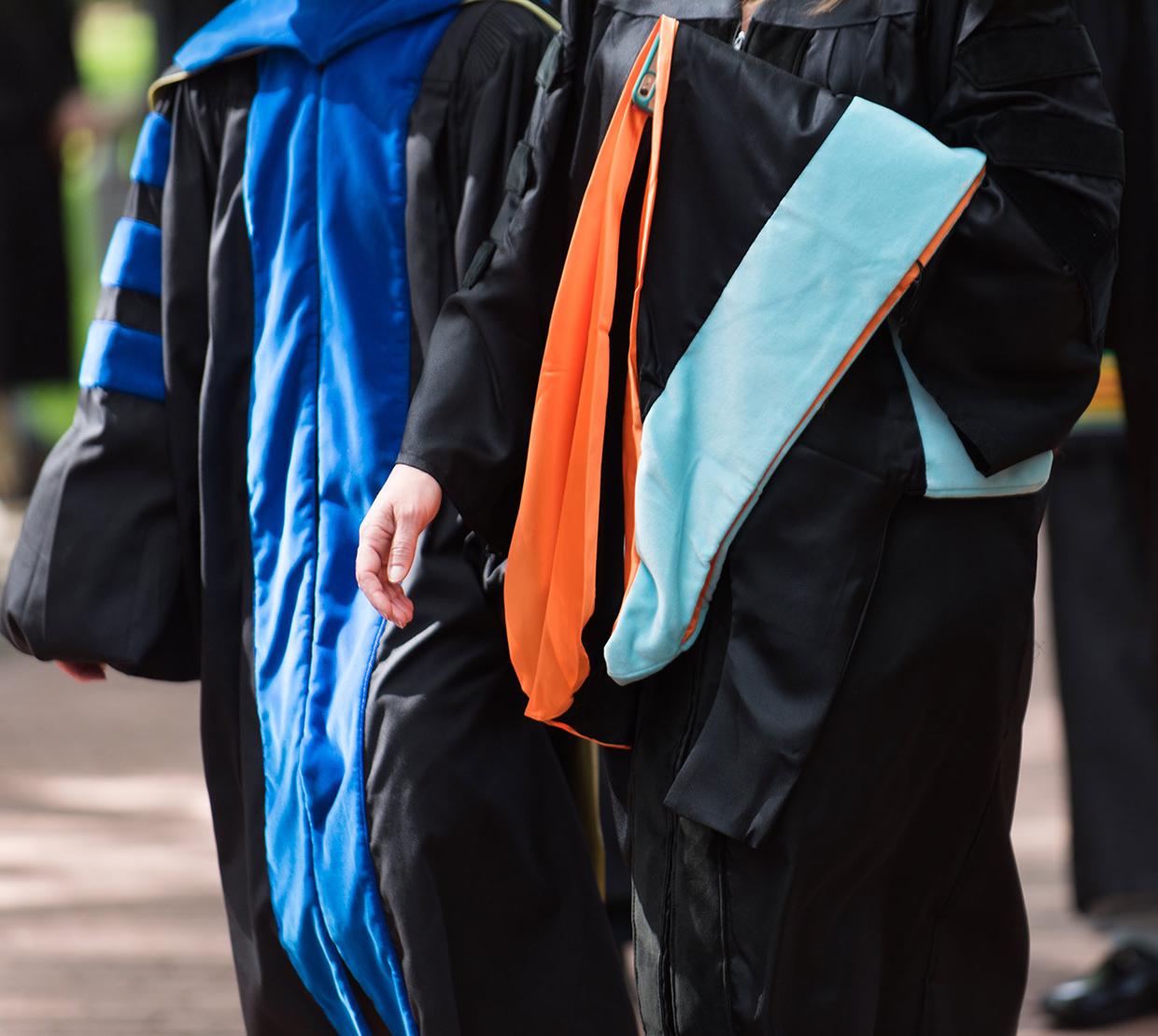 Two professors walking in doctoral gowns on campus
