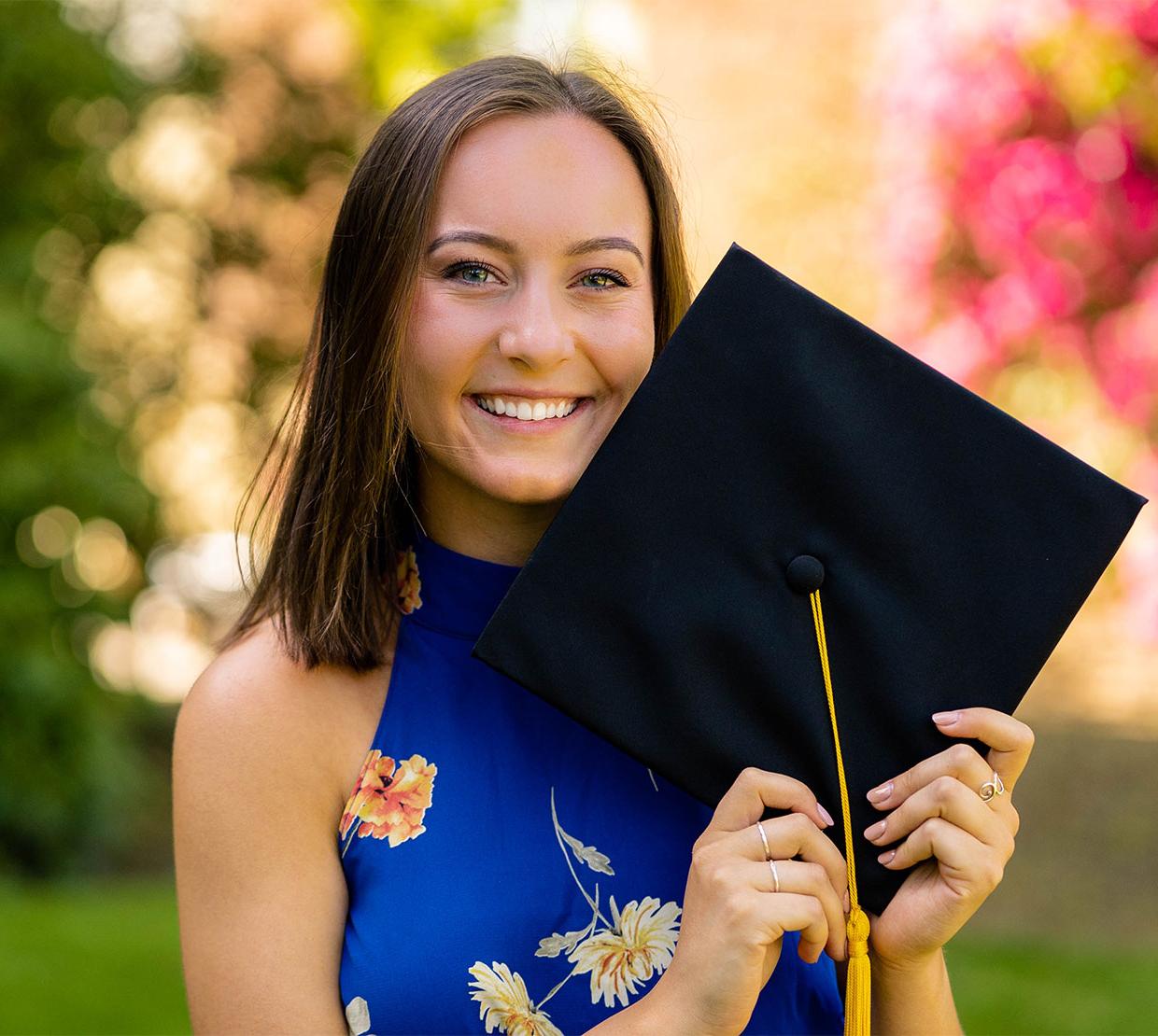 Jade Sentker holding graduation cap in front of shrubbery
