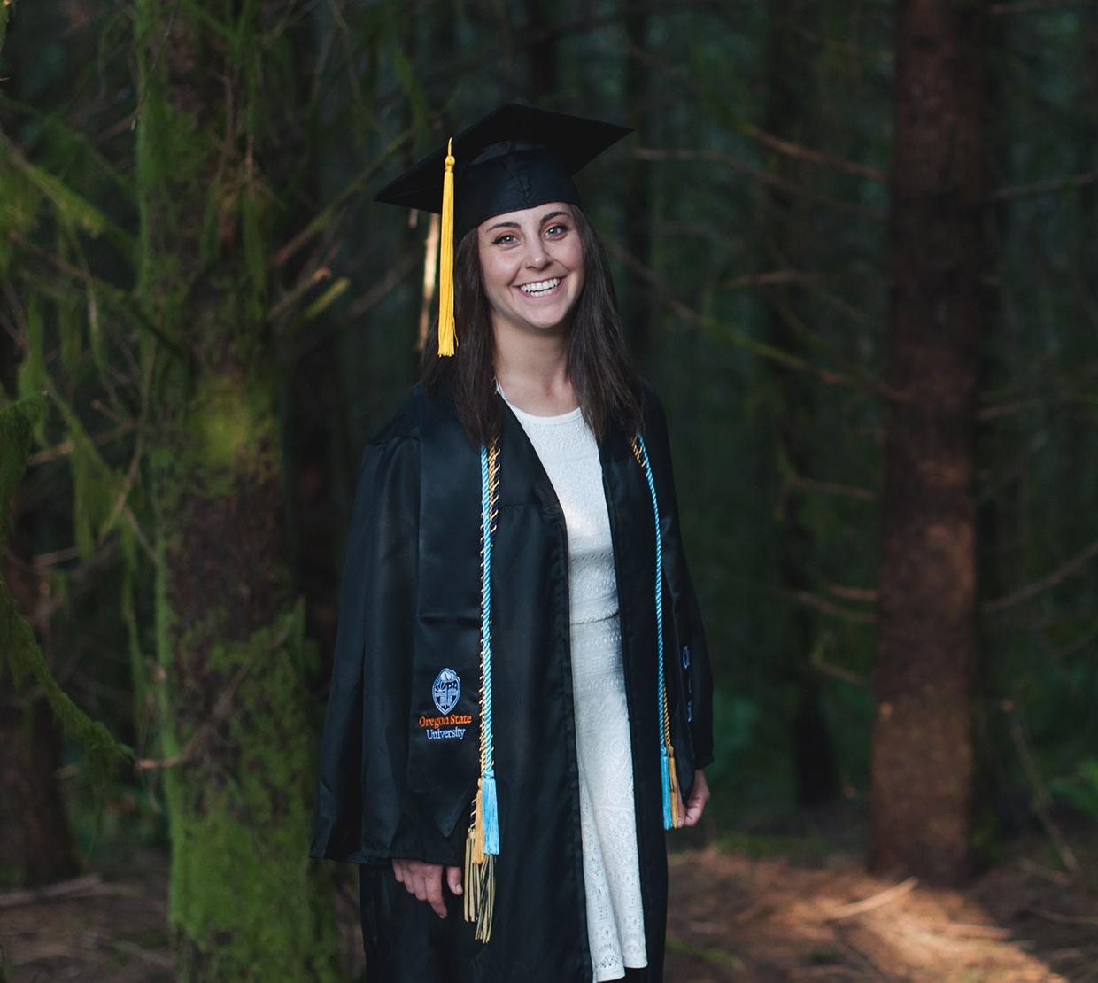 Taylor Robinson in graduation gown, standing in forest