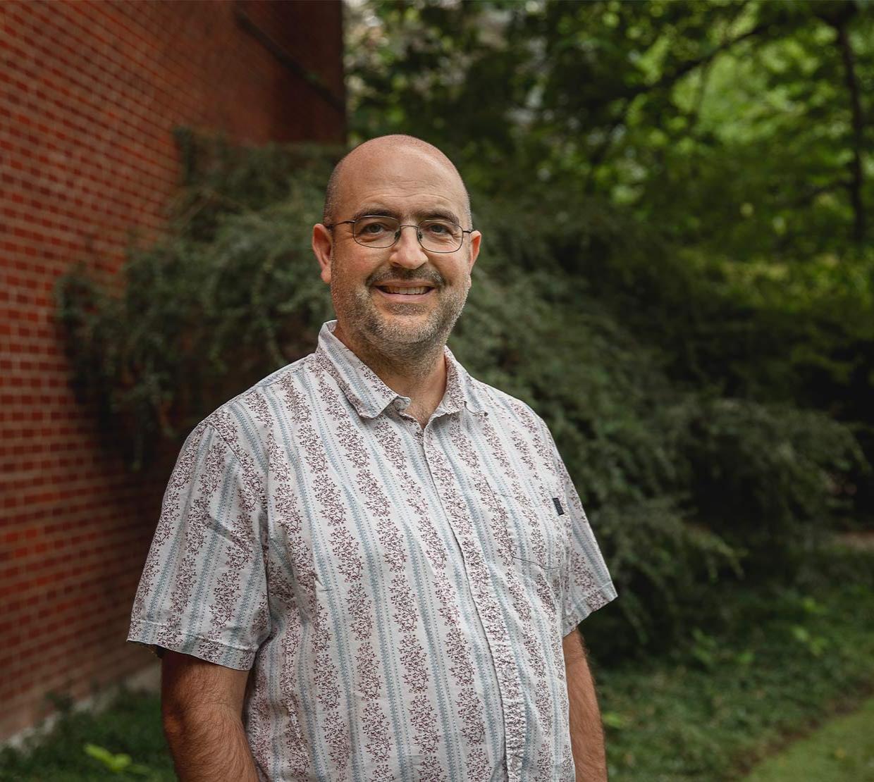 Dee Denver standing in front of a brick wall and shrubbery on OSU's Corvallis campus.