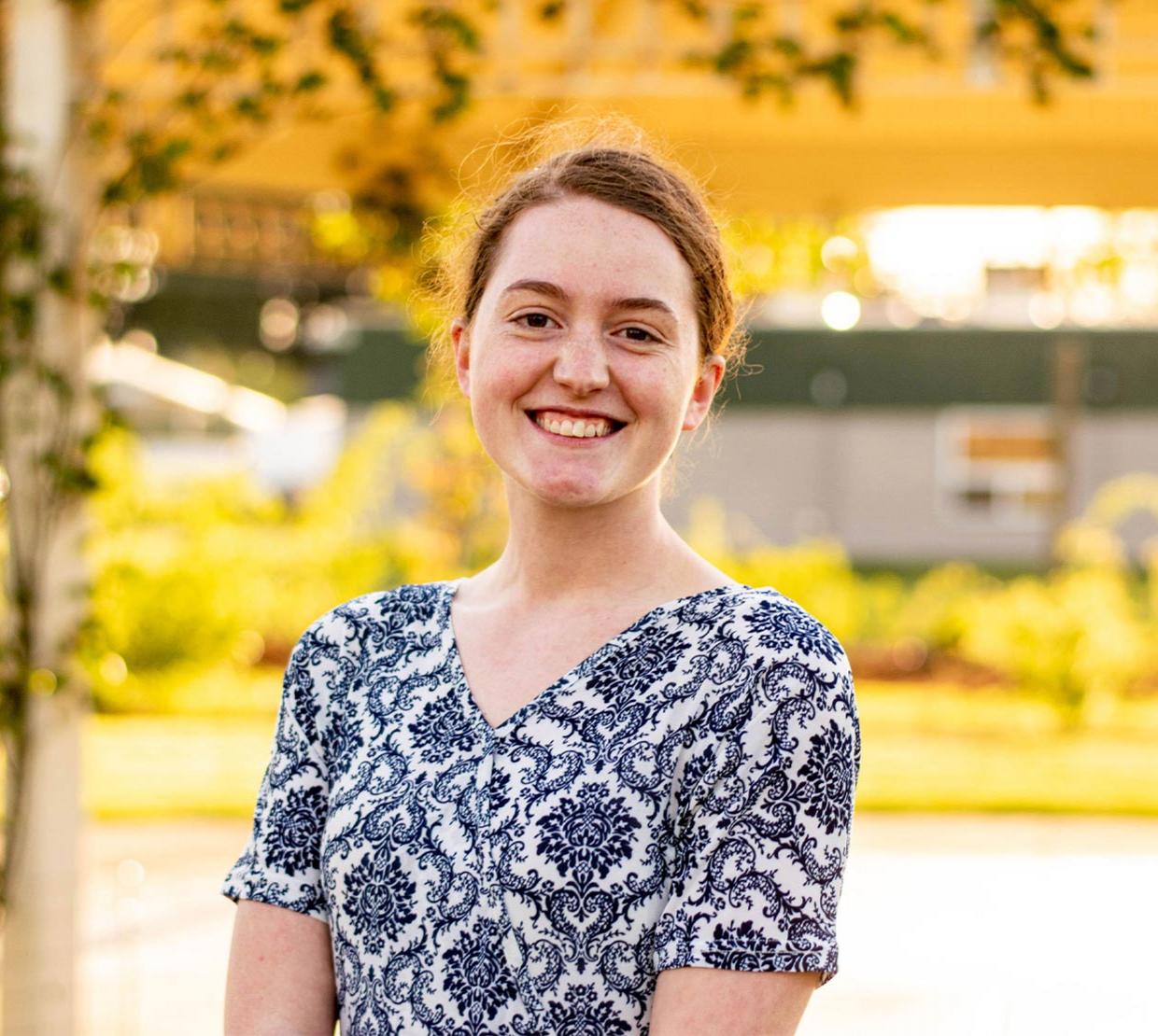 A smiling girl posing in front of of a yellow background outdoors