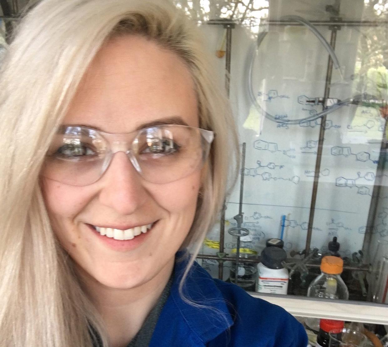 Blonde woman with clear eye protection smiling in a laboratory setting