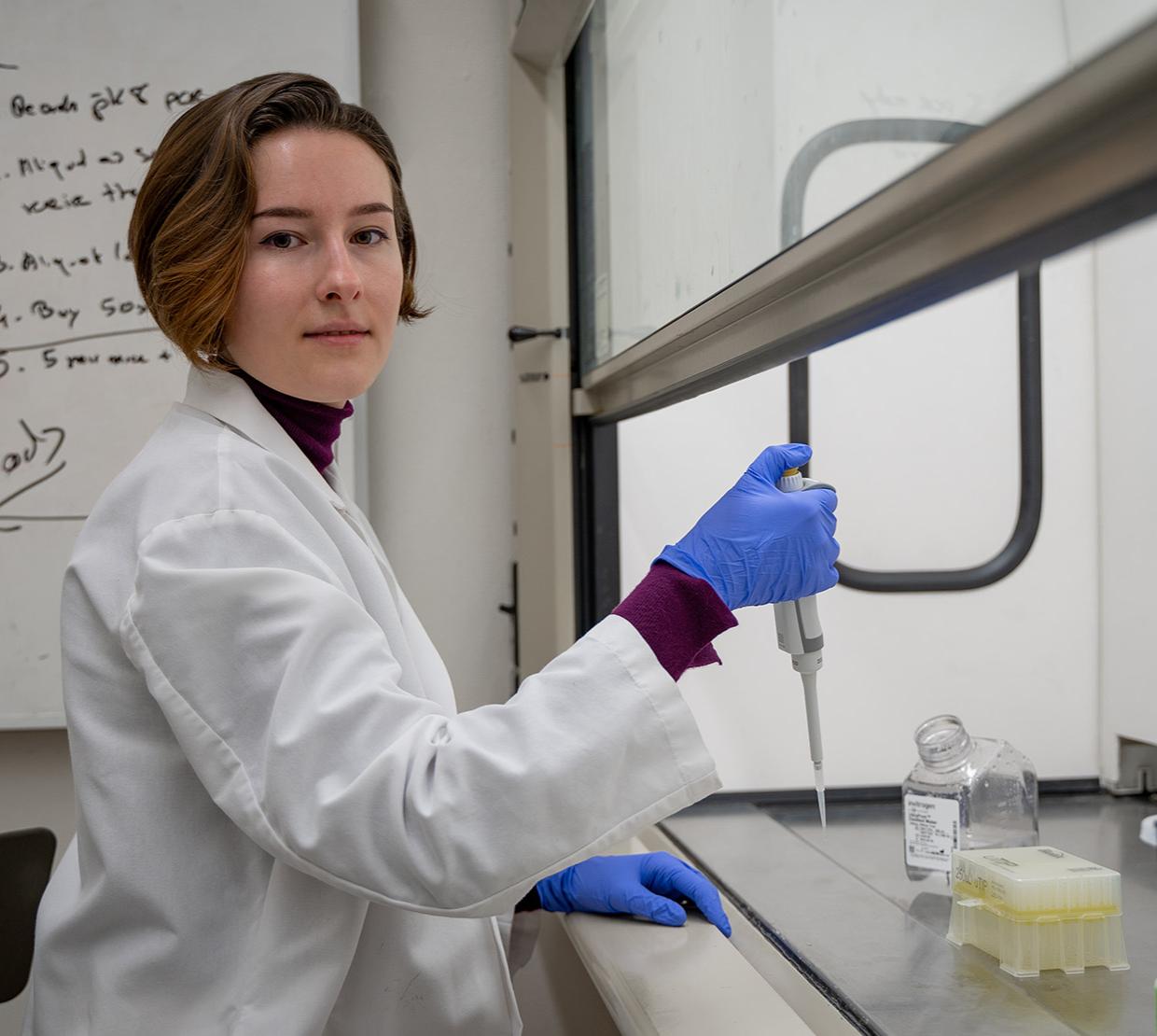 Elizaveta Zhivaya in a lab wearing a lab coat holding a pipette.