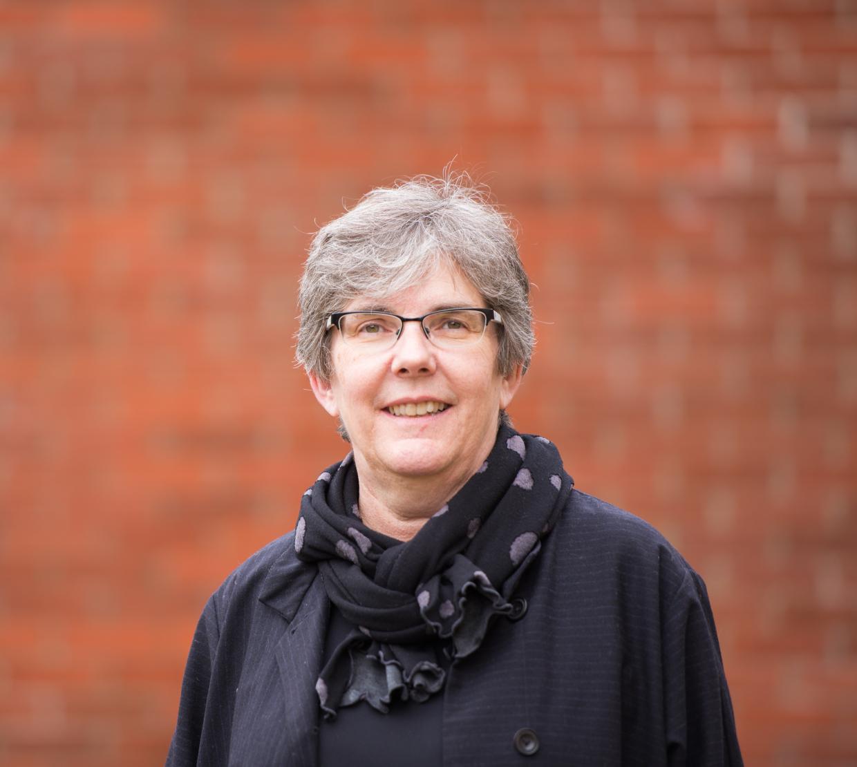 A woman in glasses standing in front of a brick wall