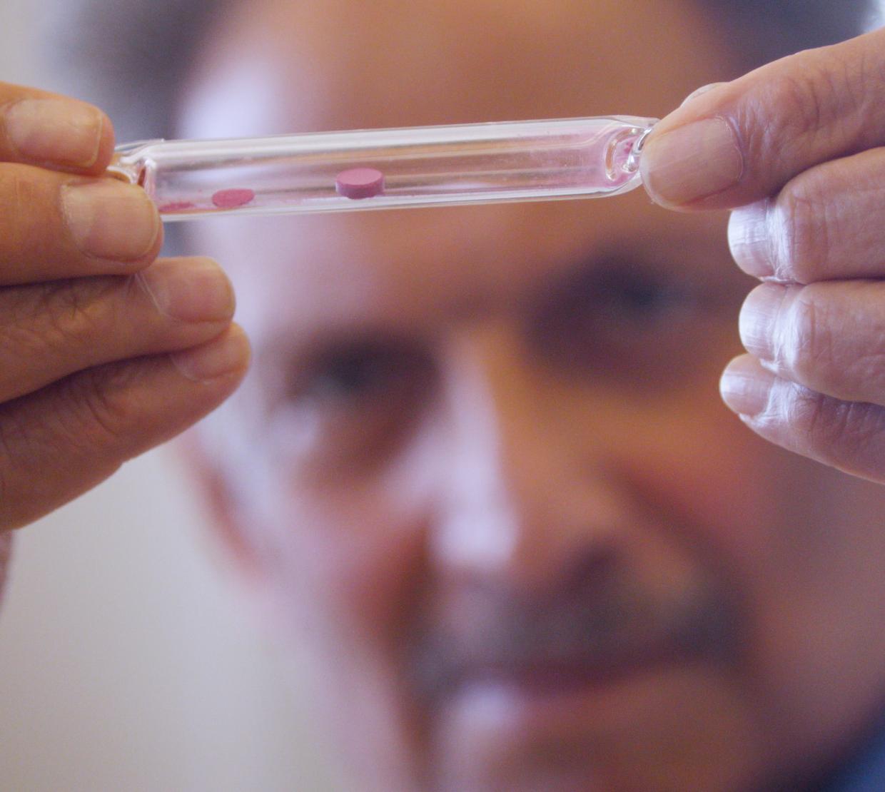 A man in a lab coat holds a vial with a red pigment.
