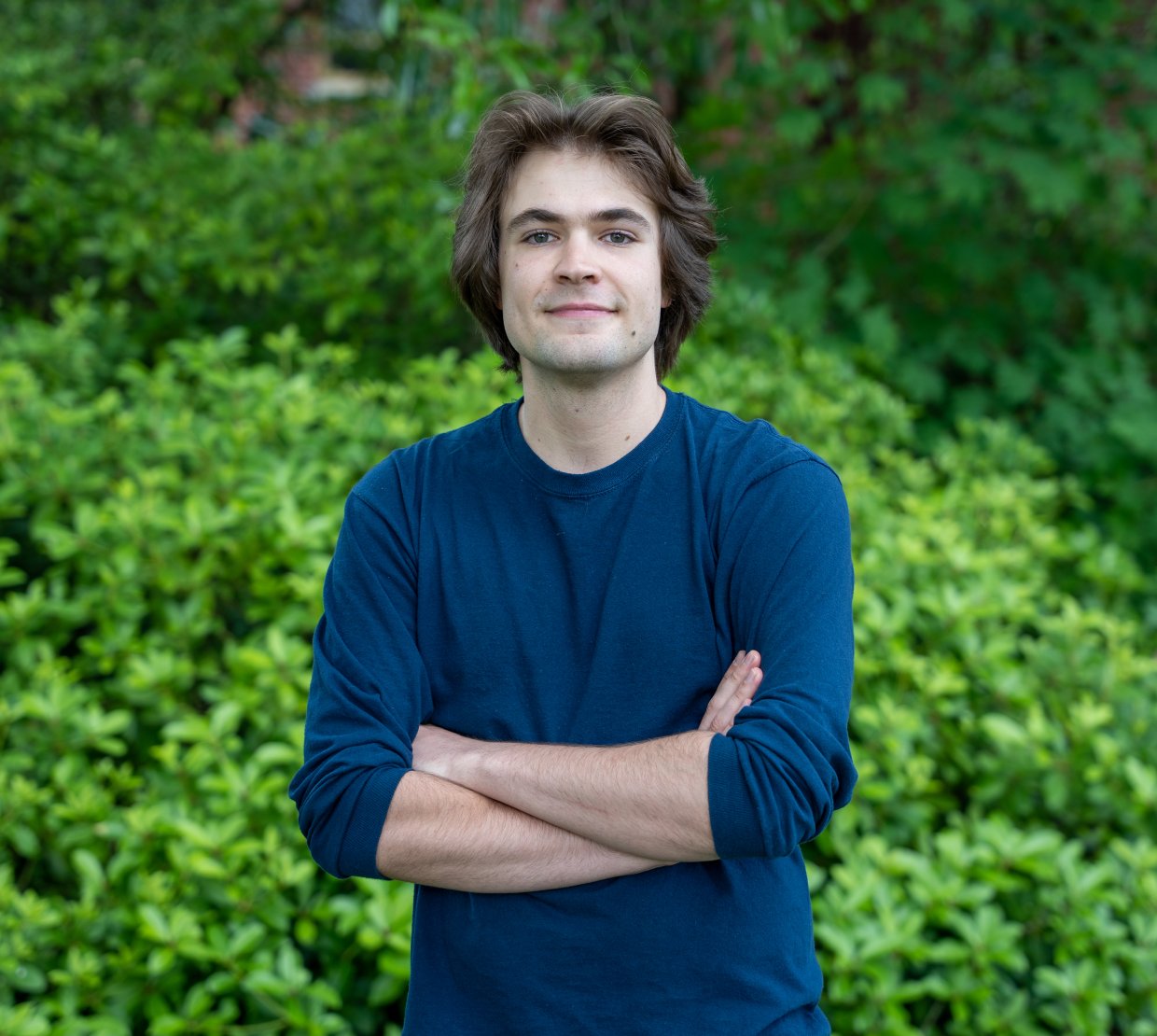 Joey Takach posing with a smile in front of leafy green bushes.