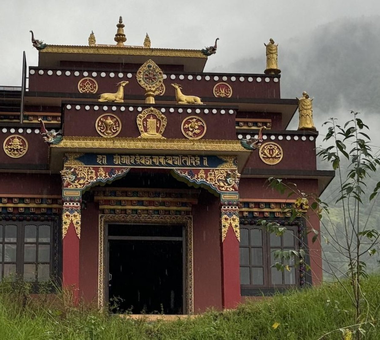 A red and gold Nepalese temple situated among misty green mountains.