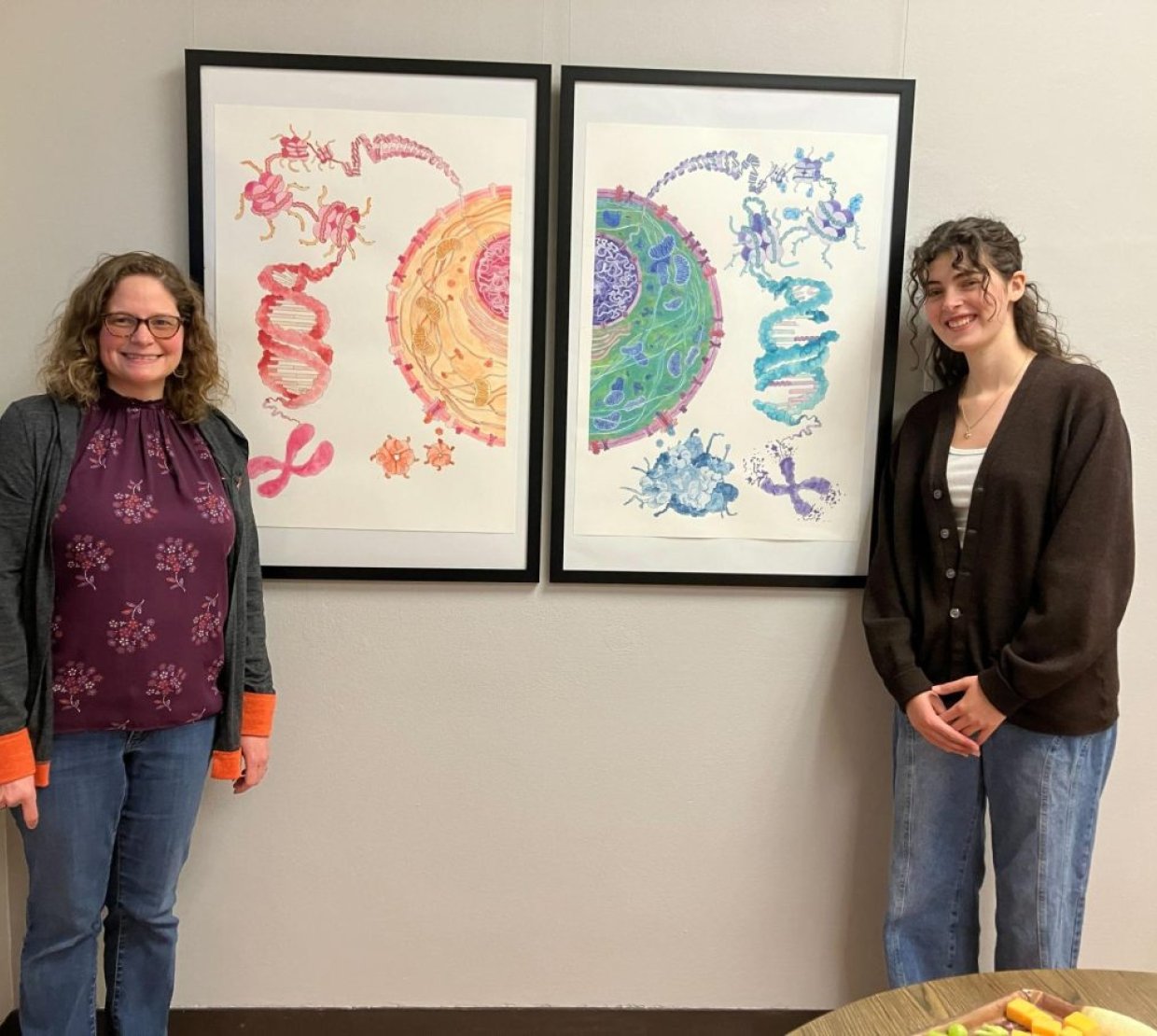 AJ Damiana and Alysia Vrailas-Mortimer pose next to Damiana's yellow, green, red, and blue painting, split between two frames.