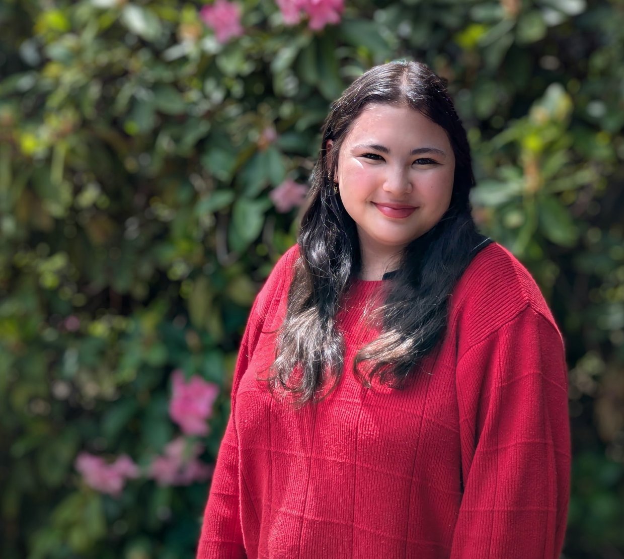 Emily Kaneshiro smiles in front of flowery bushes.