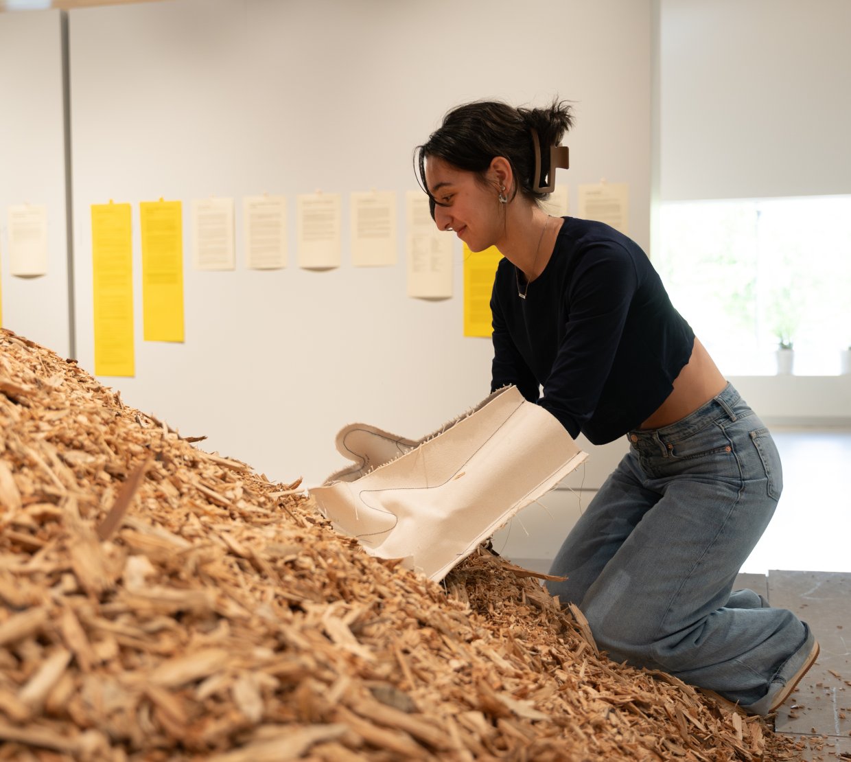 Woman uses gloves to sift through pile of wood chips in art exhibit