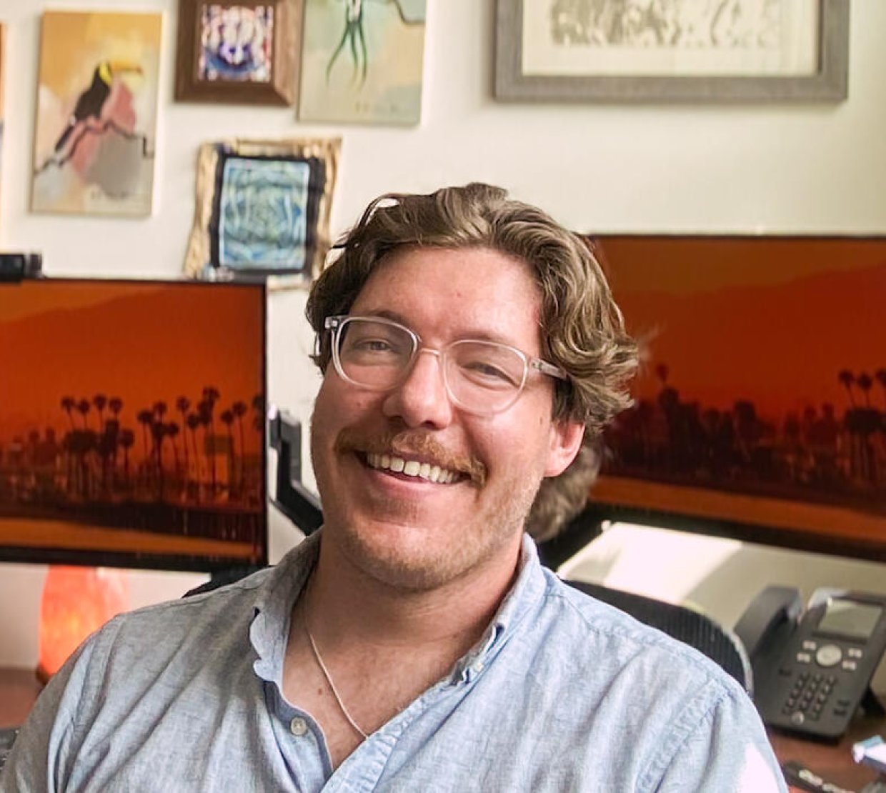 A man sits in an office with computer screens behind him.