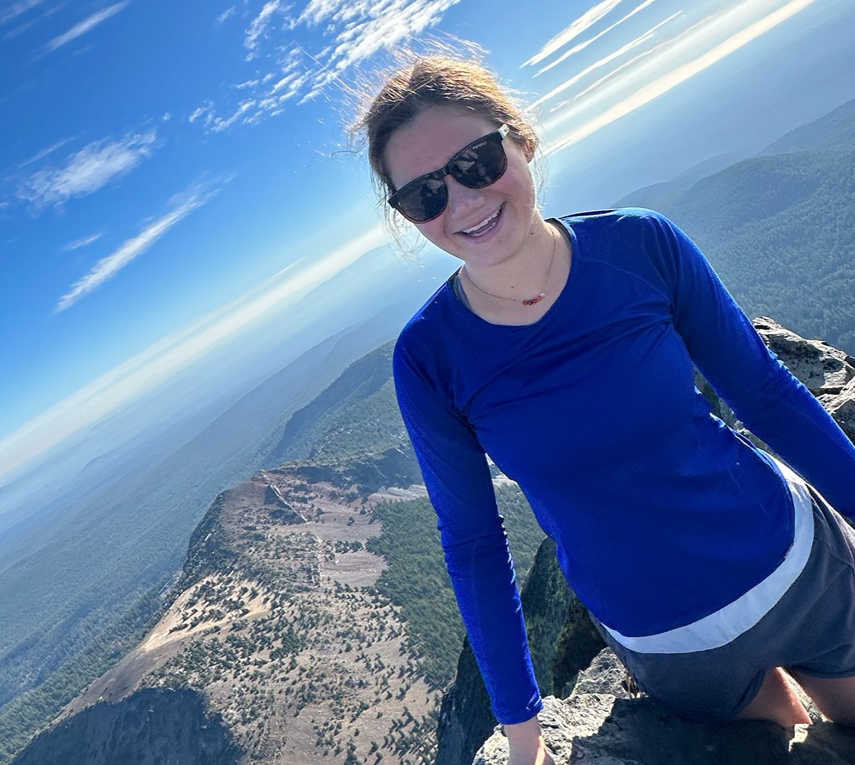 A woman in a blue shirt on top of a mountain.
