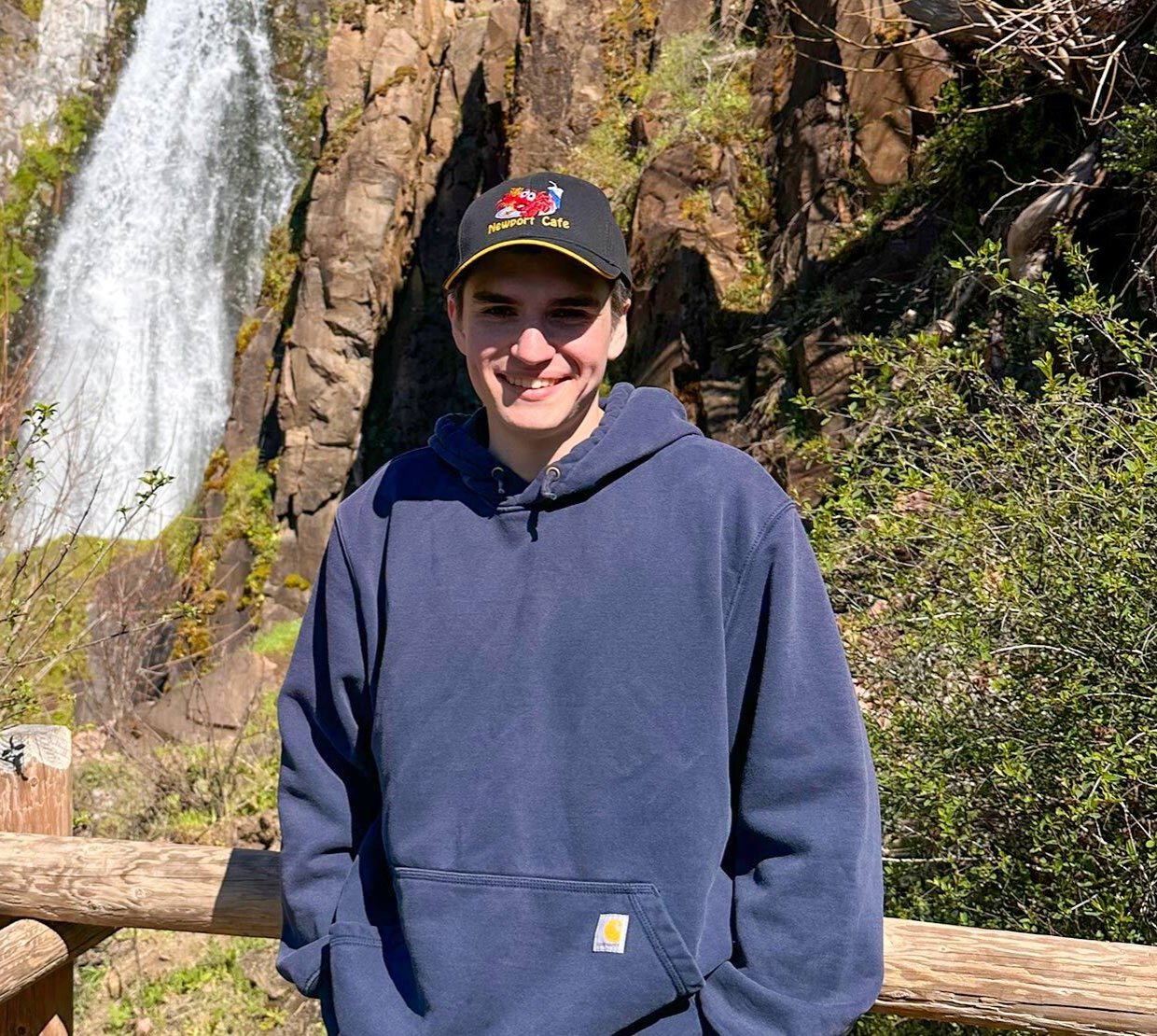 A man stands in front of a waterfall.