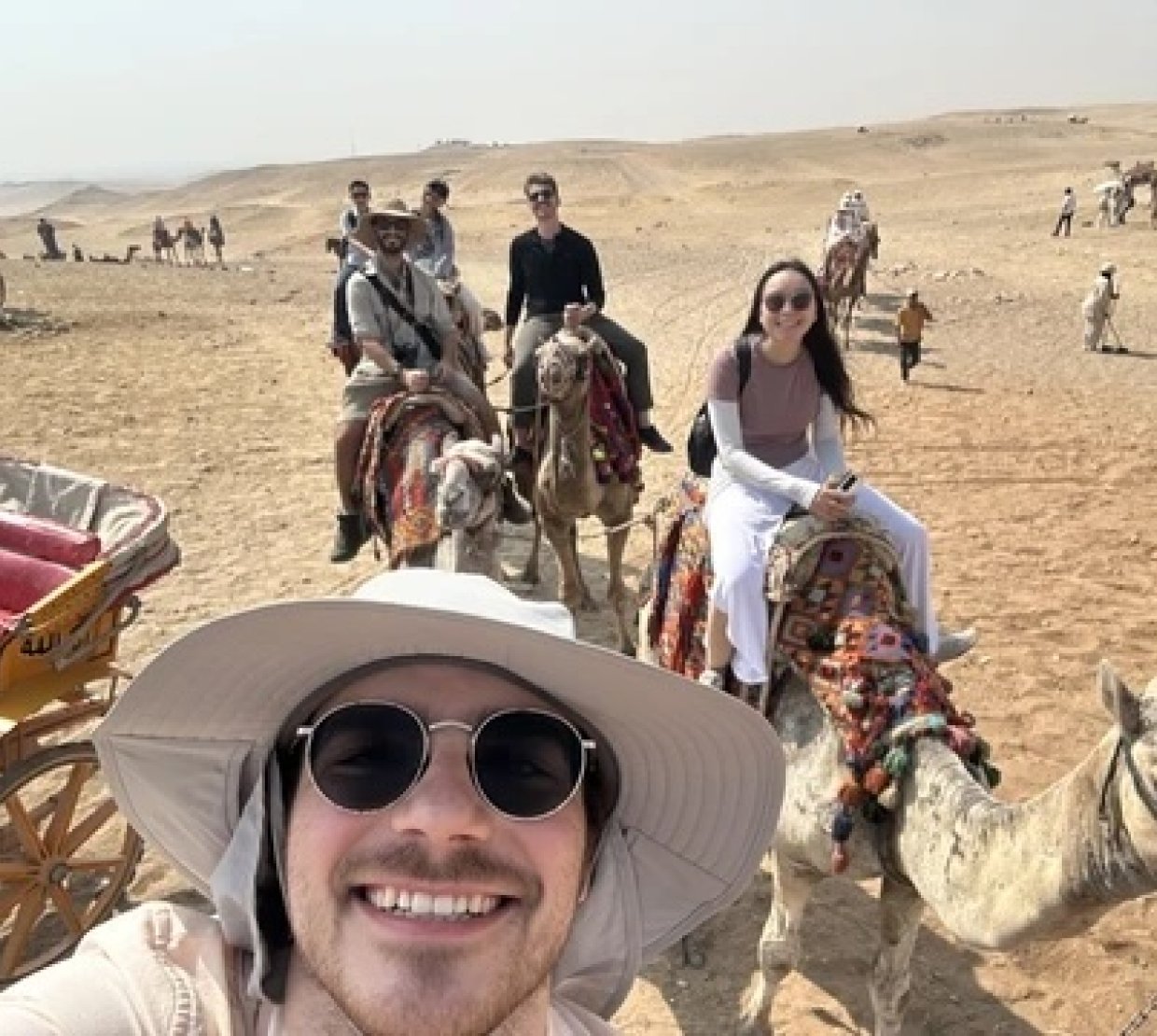 A man in a hat poses while riding a camel.