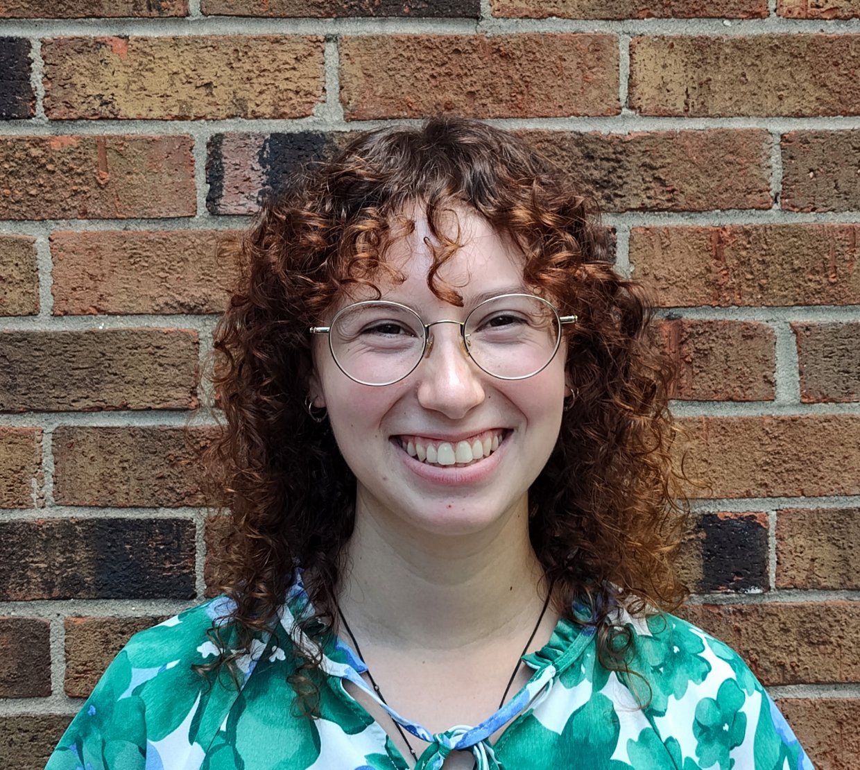A woman with red hair poses for a picture in front of a brick wall.