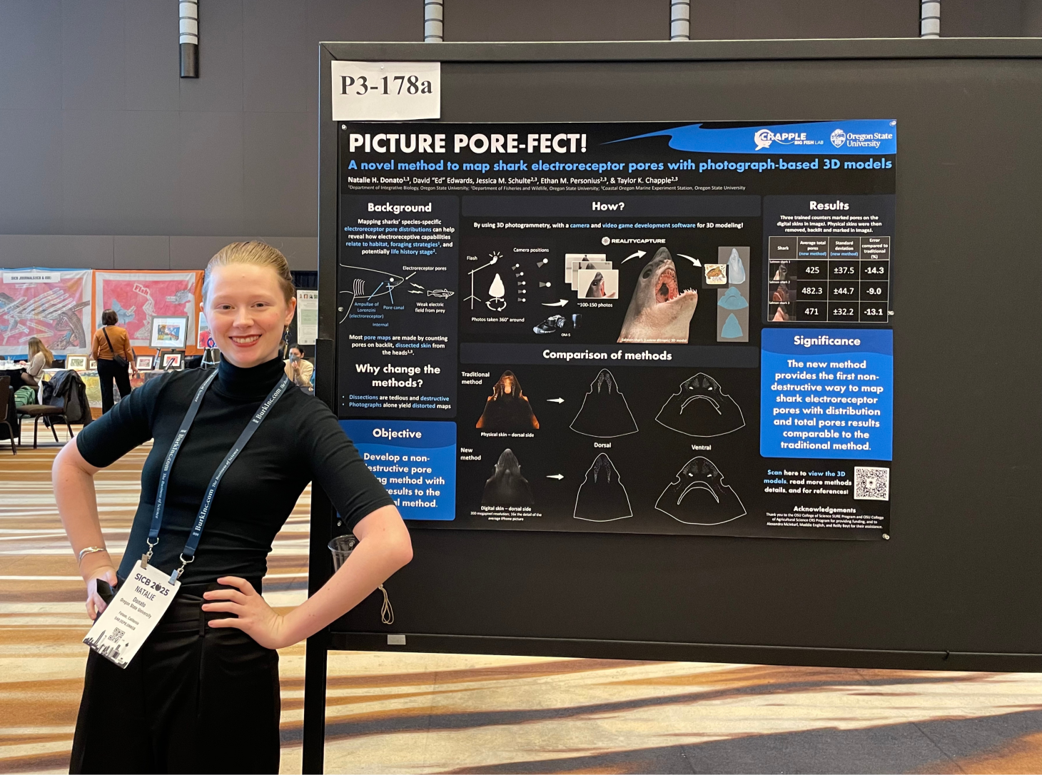 Natalie Donato smiles in front of her "Picture Pore-fect" research poster filled with blue and black details on how to map electroreceptor pores from 3D shark models.