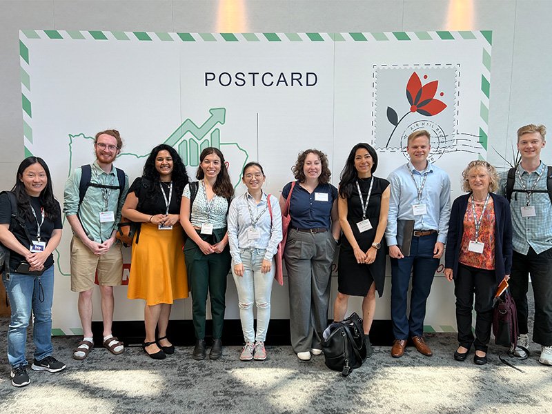 Oregon State statistics faculty and students at the JSM in front of a giant mural of a postcard.