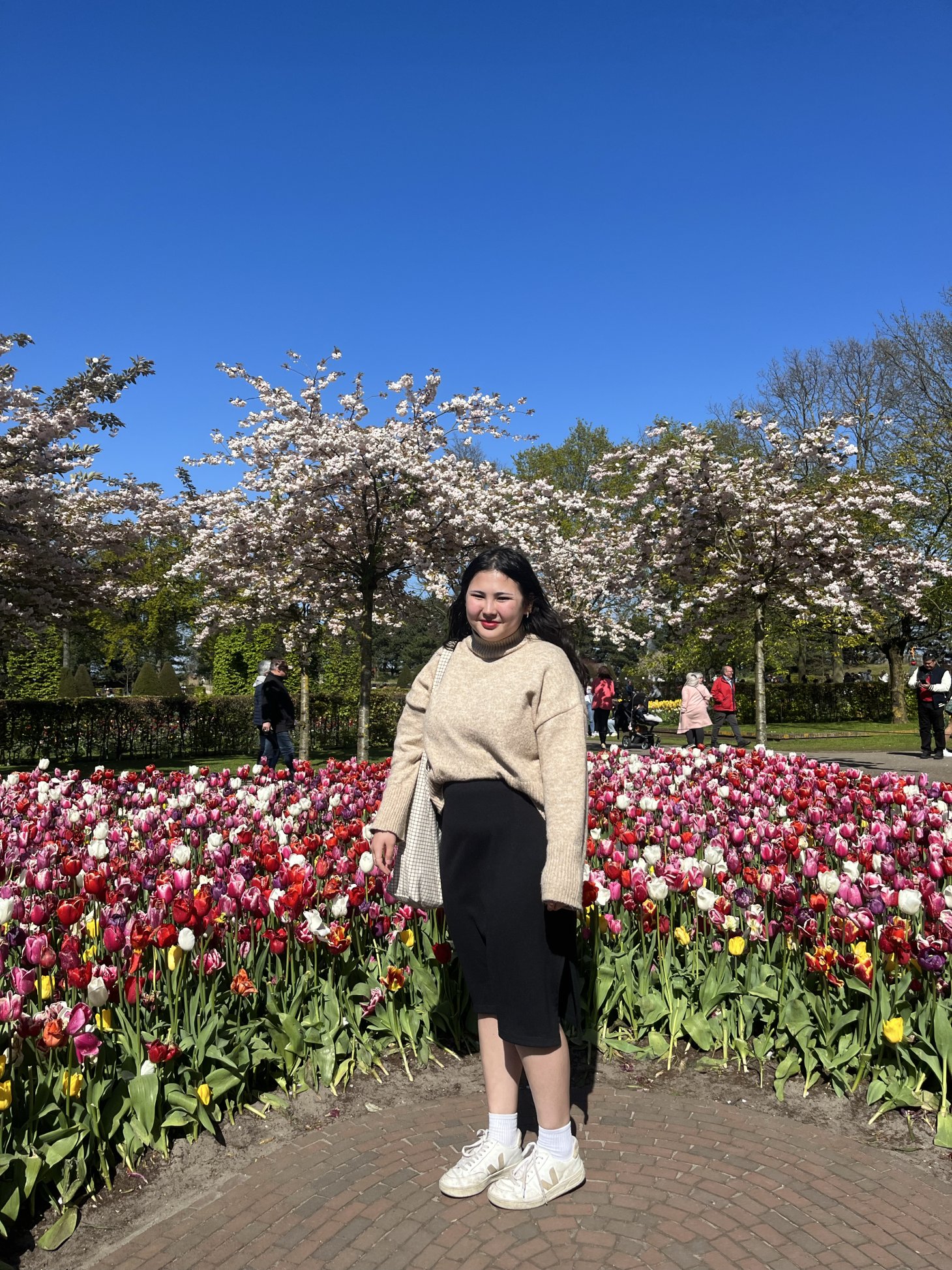 Emily Kaneshiro smiles outside in front of rows of pink, red, and white roses.