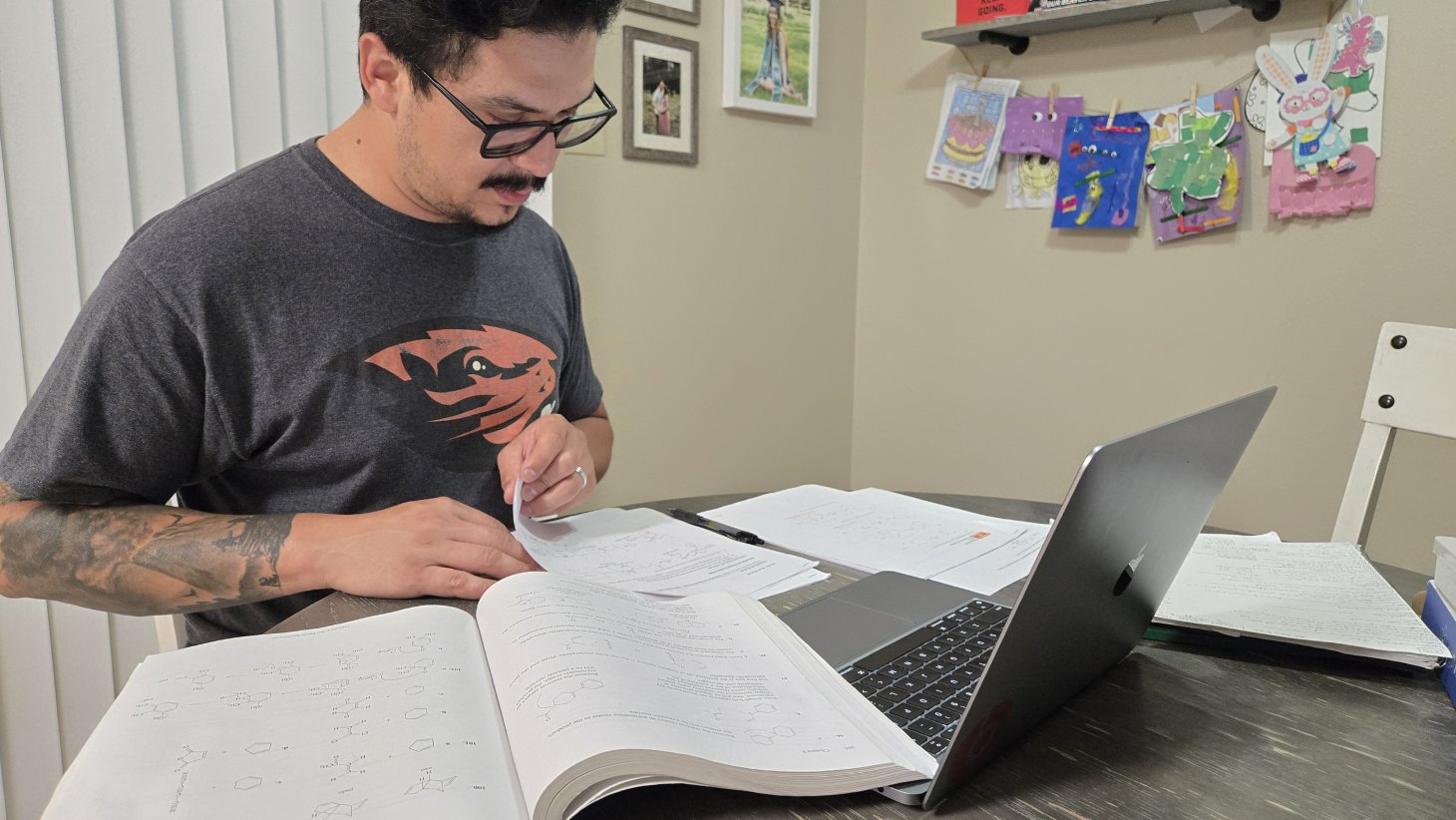 Esteban Contreras studies at the table with textbooks and papers sprawled in front of a computer.