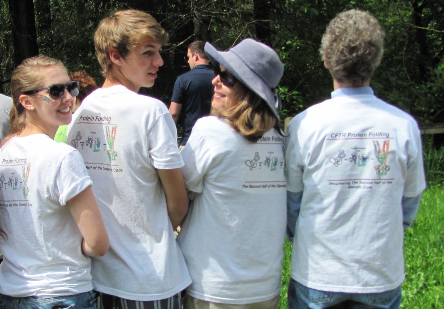 Skach and his family stand with their backs to the camera. They are wearing white shirts with colorful CFTR protein folding graphics.
