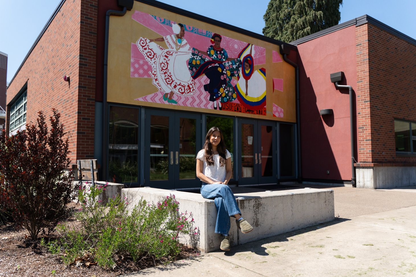 Maria Ruiz Cortes sits outside under beautiful artwork on the side of El Centro Cultural.